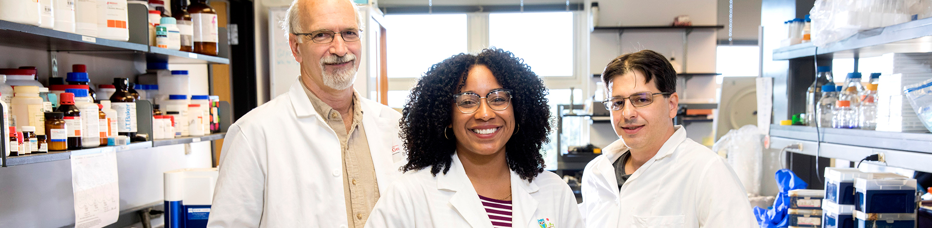 three researchers wearing white coats posing for camera